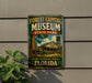 A vintage-style sign for the Forest Capital Museum in State Park, Florida, featuring an illustration of a museum building and a wagon.