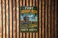 A vintage-style metal sign for Fort Abraham Lincoln State Park in North Dakota, featuring a cannon and a wooden building in the background.
