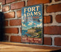 A vintage-style metal sign for Fort Adams State Park in Rhode Island, featuring a castle and a serene landscape, is displayed on a brick wall.