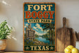 A vintage-style sign for Fort Boggy State Park in Texas, featuring a scenic landscape with a river, palm trees, and wildlife.