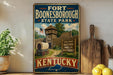 A vintage-style sign for Fort Boone, Kentucky State Park, featuring a wooden fort with a tower and a wagon, surrounded by trees and a wooden fence.