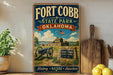 A vintage-style metal sign for Fort Cobb State Park in Oklahoma, featuring a cannon, a building, and a sign that reads "Fort Cobb State Park - Oklahoma".