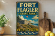 A vintage-style sign for Fort Flagler State Park in Washington, featuring an illustration of the park's landscape and a flag flying atop a building.