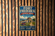 A vintage metal sign for Fort Frederick State Park in Maryland, featuring an illustration of a castle and a cannon, mounted on a wooden wall.