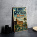 A vintage-style sign for Fort George Island, Florida, featuring a castle and palm trees, is displayed on a gray countertop next to a stack of black camera lenses.