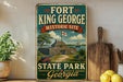 A vintage-style sign for Fort King George Historic Site in Georgia, featuring a painting of a historic fort surrounded by palm trees and other natural scenery.