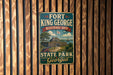 A vintage metal sign for Fort King George Historic Site in Georgia, featuring a scenic illustration of the historic site with a wooden fence and a ship in the background.