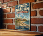 A vintage-style metal sign for Fort Macon State Park in North Carolina, featuring a coastal landscape with a castle, beach, and ocean.