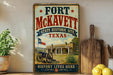 A vintage-style metal sign for Fort McKeett, Texas, featuring a cannon and a historic building, is displayed on a shelf next to a wooden cutting board and some lemons.