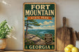 A vintage-style sign for Fort Mountain State Park in Georgia, featuring a scenic landscape with a mountain, pine trees, and a river.