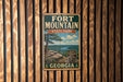 A vintage metal sign for Fort Mountain State Park in Georgia, featuring a scenic landscape with a pine tree and mountains in the background.