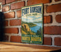 A vintage-style metal sign for Fort Ransom State Park, featuring a scenic landscape with a lake and mountains in the background.