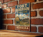 A vintage-style metal sign for Fort Robinson State Park in Nebraska, featuring an illustration of the park's historic buildings and a prominent American flag.