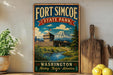 A vintage-style sign for Fort Simcoe State Park in Washington, featuring a castle, mountains, and a river, is displayed on a wooden shelf next to a potted plant and a cutting board.