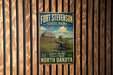 A vintage metal sign for Fort Stevenson State Park in North Dakota, featuring a cannon and a wooden fence, mounted on a wooden wall.