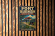 A vintage-style metal sign for Fort Washington State Park in Pennsylvania, featuring an illustration of a cannon and a building, mounted on a wooden fence.