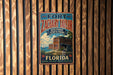 A vintage-style metal sign for Fort Zachary Taylor Historic State Park in Florida, featuring a tropical beach scene with palm trees and a cannon.