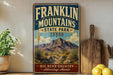 A vintage Franklin Mountains State Park sign is displayed on a shelf, with a potted plant and a cutting board nearby.