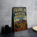A vintage Franklin Mountains State Park sign stands on a gray countertop, featuring a desert landscape with mountains and a cactus in the background.
