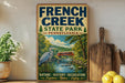 A vintage-style sign for French Creek State Park in Pennsylvania, featuring an illustration of a heron and a bridge over a river.