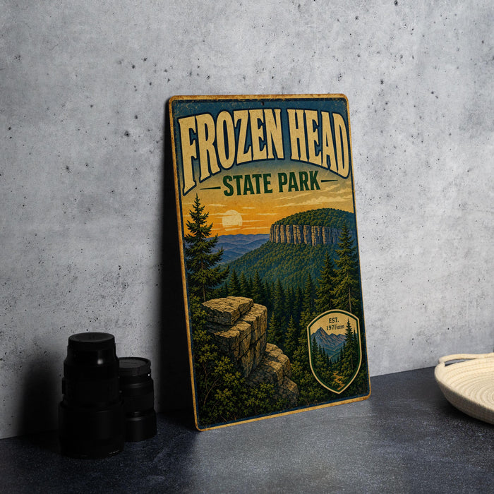 A vintage-style sign for Frozen Head State Park, featuring a scenic mountain landscape with pine trees and a sunset in the background.