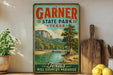 A vintage-style sign for Garnier State Park in Texas, featuring a scenic landscape with a river and mountains.