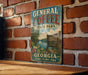 A vintage-style metal sign for General Coffee State Park in Georgia, featuring a scenic landscape with a lake and trees.