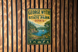 A vintage-style metal sign for George Wyth Memorial State Park in Iowa, featuring a scenic landscape with a lake, mountains, and a sailboat.