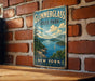 A vintage-style metal sign for Glimmerglass State Park in New York, featuring a scenic landscape with a lake, mountains, and a sailboat.
