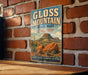 A vintage metal sign for Gloss Mountain State Park in Oklahoma, featuring a desert landscape with mountains and desert plants.