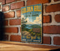 A vintage-style metal sign for Golden Hill State Park, featuring a scenic landscape with a river and mountains, mounted on a brick wall.