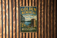 A vintage-style metal sign for Golden Memorial State Park in Mississippi, featuring a scenic landscape with a lake, trees, and a monument.