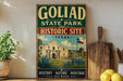 A vintage-style sign for Goliad State Park and Historic Site in Texas, featuring an illustration of the historic Alamo and surrounding landscape.