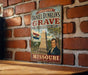 A vintage metal sign for Daniel Dunlin's Grave, a state historic site in Missouri, mounted on a brick wall.