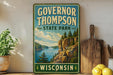 A vintage-style sign for Governor Thompson State Park in Wisconsin, featuring a scenic landscape with a lake and mountains.