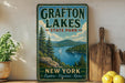 A vintage-style sign for Grafton Lakes State Park in New York, featuring a scenic landscape with a lake surrounded by mountains and pine trees.