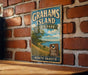A vintage metal sign for Grahams Island State Park in North Dakota, featuring a scenic landscape with a lake and trees.