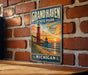 A vintage-style metal sign for Grand Haven State Park in Michigan, featuring a lighthouse and a sunset over the ocean.