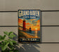 A vintage-style metal sign for Grand Haven State Park in Michigan, featuring a lighthouse and a sunset over the ocean.