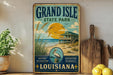 A vintage-style metal sign for Grand Isle State Park in Louisiana, featuring a beach scene with a house, palm trees, and a bird.