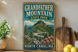 A vintage-style sign for Grandfather Mountain State Park in North Carolina, featuring a scenic mountain landscape with a winding road and pink flowers.