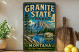 A vintage-style metal sign for Granite State Park in Montana, featuring a mountain landscape and a river.