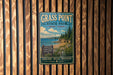 A vintage-style metal sign for Grass Point State Park in New York, featuring a scenic landscape with pine trees, a beach, and a body of water.