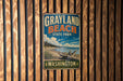 A vintage metal sign for Grayland Beach State Park in Washington, featuring a scenic landscape with a beach, mountains, and a clear blue sky.