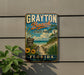 A vintage-style metal sign for Grayton Beach State Park in Florida, featuring a beach scene with palm trees, a sandy path, and a blue sky with clouds.
