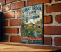 A vintage-style metal sign for Great Brook Farm State Park in Massachusetts, featuring a scenic illustration of a farm and a river.