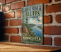 A vintage-style metal sign for Great River Bluffs State Park in Minnesota, featuring a scenic landscape with a river, mountains, and a bird in flight.
