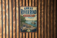 A vintage-style metal sign for Great River Road State Park in Mississippi, featuring a scenic illustration of a river, trees, and a steamboat.