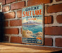 A vintage-style metal sign for Great Salt Lake State Park in Utah, featuring a scenic landscape with mountains, water, and a beach.
