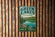 A vintage-style metal sign for Green Lakes State Park in New York, featuring a scenic image of the lake surrounded by pine trees.